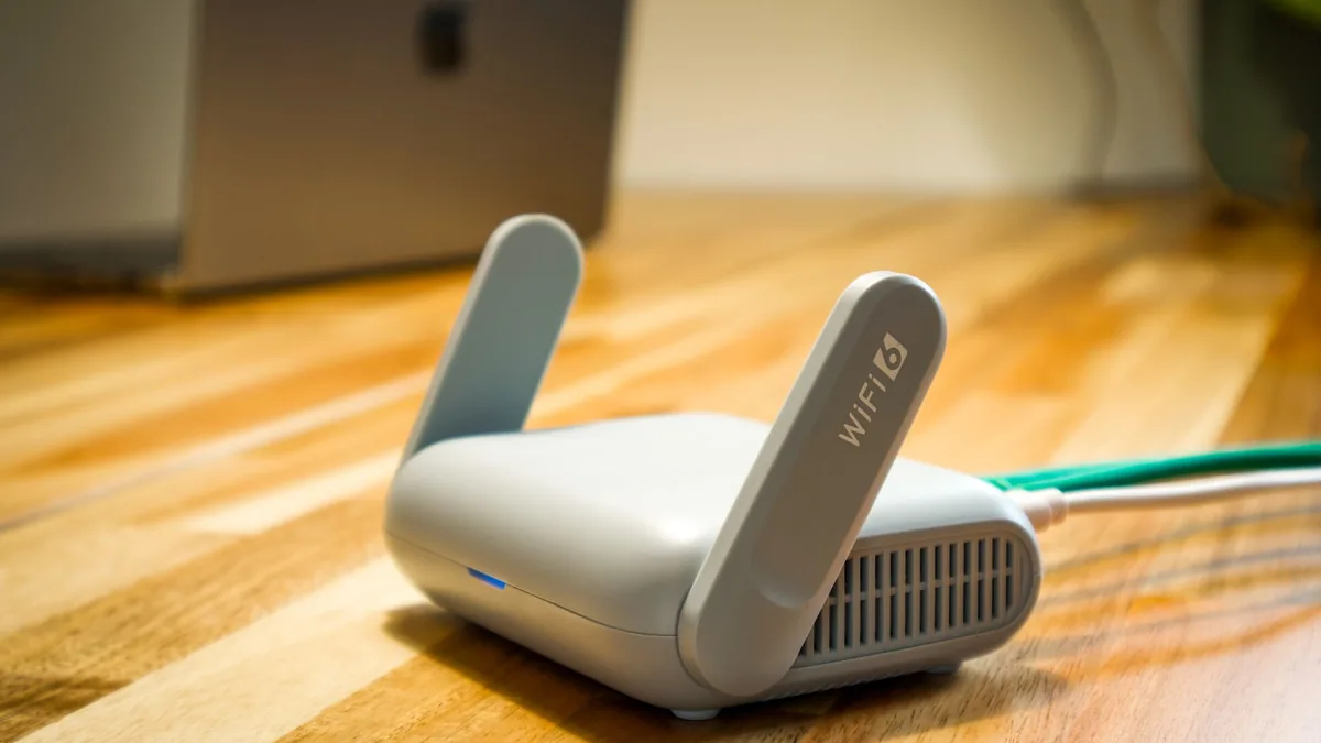 Router travel mini di atas meja kayu dengan laptop di belakangnya